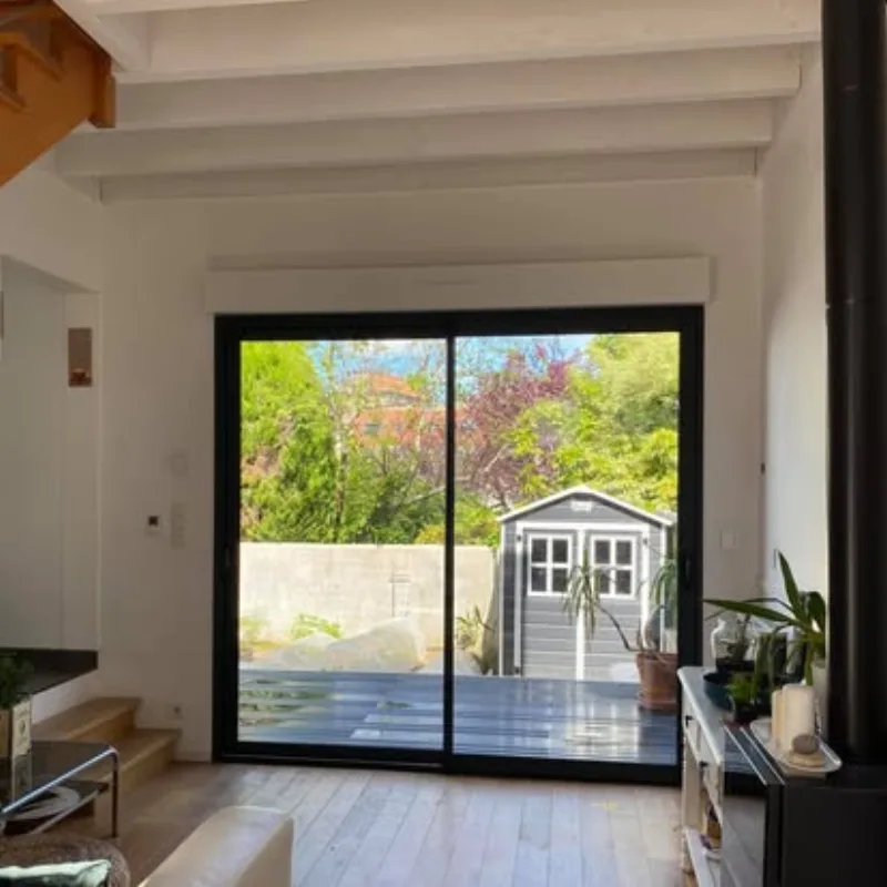 Baie vitrée coulissante aluminium noir intérieur ouvert sur jardin