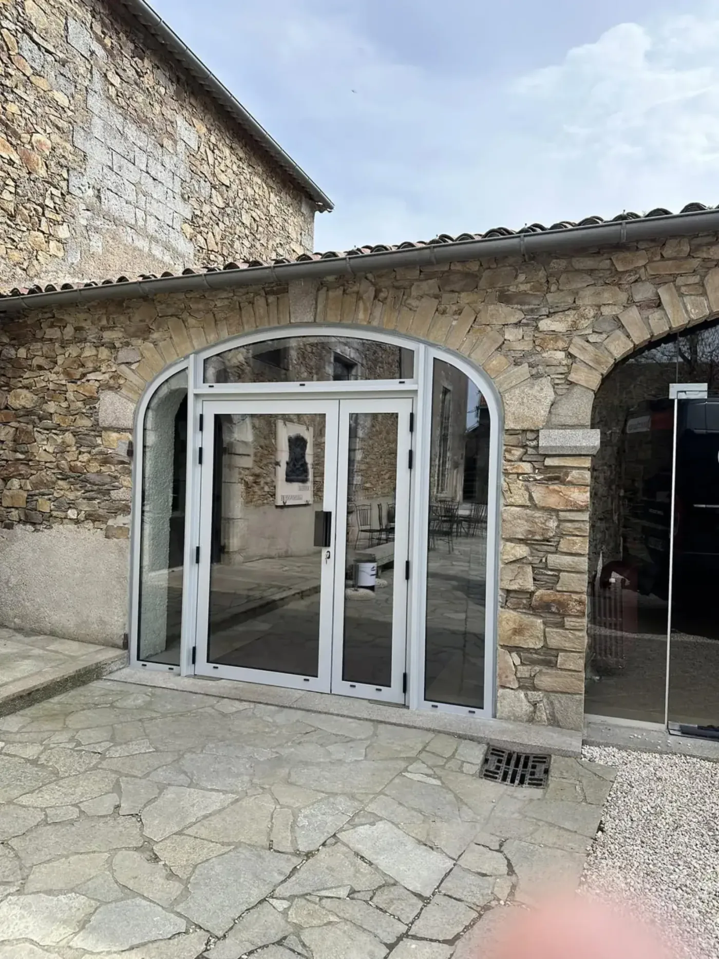 Double porte vitrée aluminium blanc cintrée sur mur en pierre