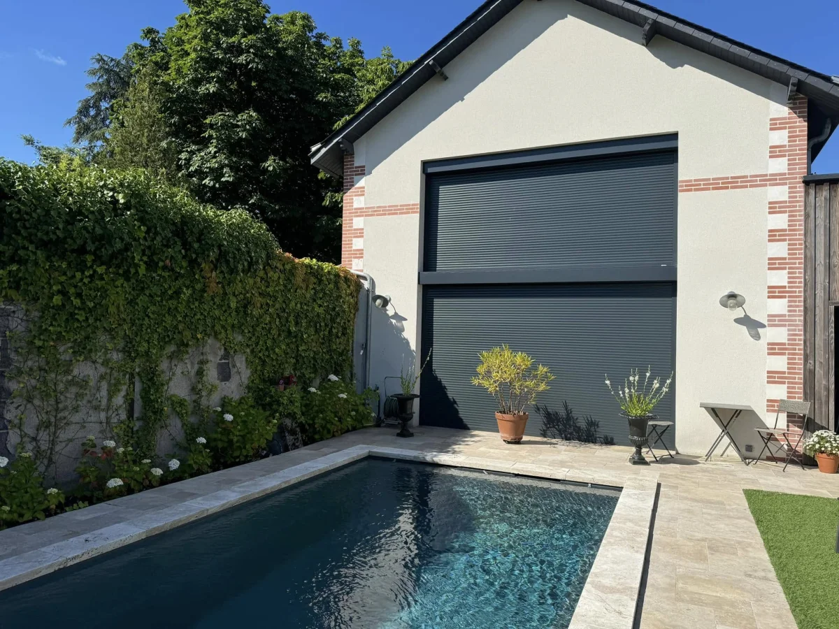 Porte de garage enroulable aluminium anthracite façade brique devant une piscine