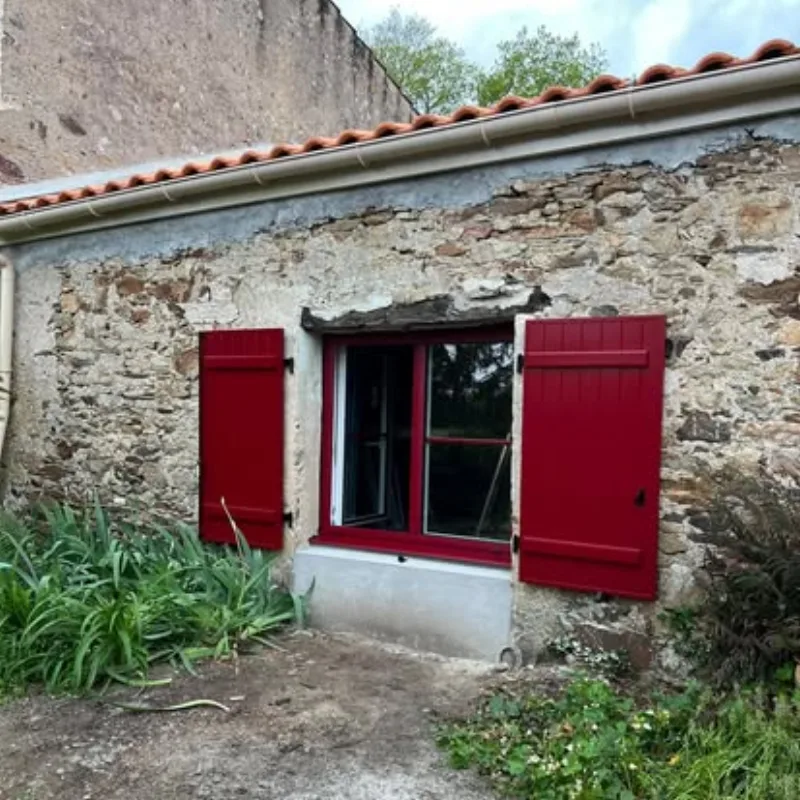 Volets battants en bois rouge sur mur en pierre apparente
